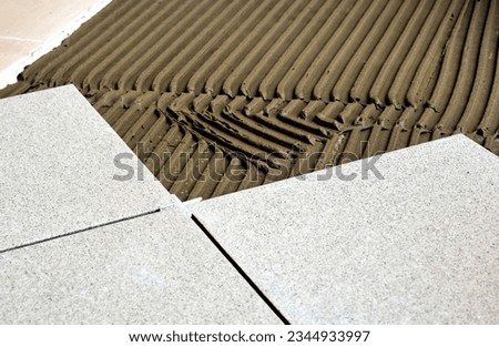 trowel on cement based grout tile base. large ceramic floor tiles. plastic or vinyl spacer. work in progress. home improvement and construction work concept. grooved troweled on cement mortar. Royalty-Free Stock Photo #2344933997