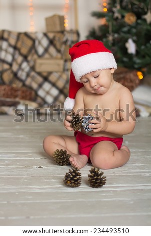 Little boy dressed as Santa sitting in front of a Christmas tree