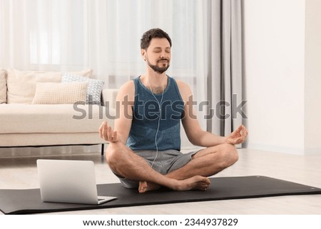 Man in sportswear meditating near laptop at home. Harmony and zen