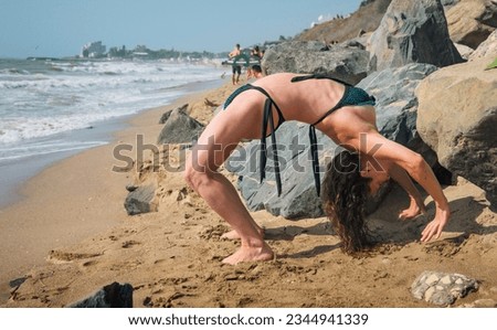 A beautiful young woman is doing yoga and gymnastics exercises on the beach. Flexibility of the human body - concept.