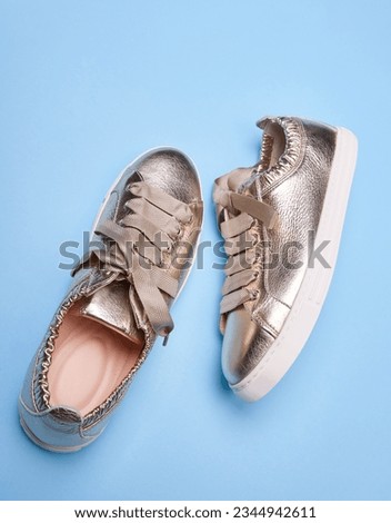 Fashionable golden metallic sneakers with wrinkled leather details and white rubber soles on a gradient blue background. Close-up view. The concept of modern stylish footwear