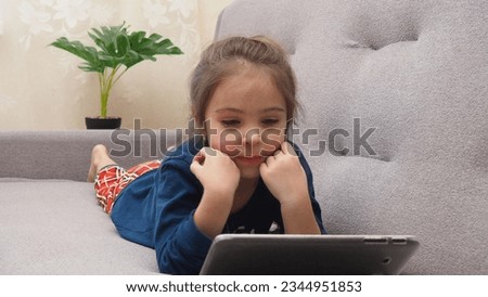 Cute little girl at home on the couch with tablet listening to audiobook at home, watching cartoons, playing games, chatting online. interactive online learning for kids