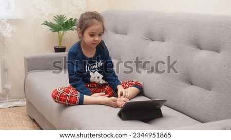 Cute little girl at home on the couch with tablet listening to audiobook at home, watching cartoons, playing games, chatting online. interactive online learning for kids