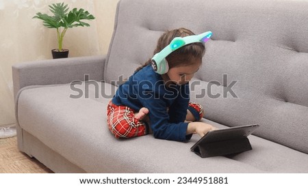 Cute little girl with headphones and tablet listening to audiobook at home, watching cartoons, playing games, chatting online. interactive online learning for kids.