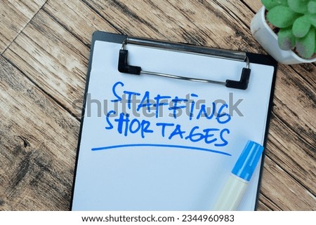 Concept of Staffing Shortages write on paperwork isolated on Wooden Table. Royalty-Free Stock Photo #2344960983