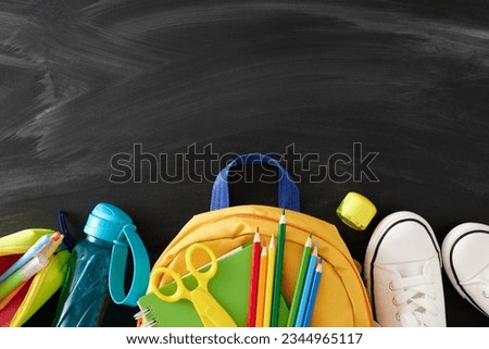 Fresh start a new school year concept. Top view flat lay of school supplies, rucksack, bottle, white shoes on blackboard background with empty space for promo or text Royalty-Free Stock Photo #2344965117