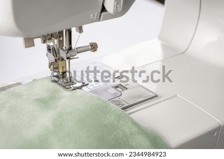 Modern sewing machine presser foot with green fabric and thread, closeup, macro. Sewing process clothes, curtains, upholstery. Business, hobby, handmade, zero waste, recycling, repair concept Royalty-Free Stock Photo #2344984923