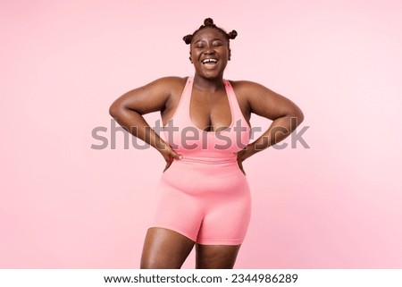 Attractive smiling African American sports woman wearing fitness uniform, bra posing for picture isolated on pink background. Nigerian female with stylish hairstyle fighting breast cancer concept