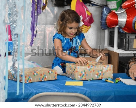 Young female girl celebrating her fifth birthday with decorations and opening presents. 