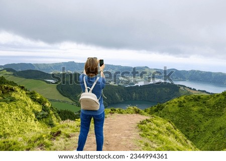 Young woman taking picture of the  beautiful landscape of the Twin Lakes in Sete Cidades in the island of Sao Miguel, Azores, Portugal