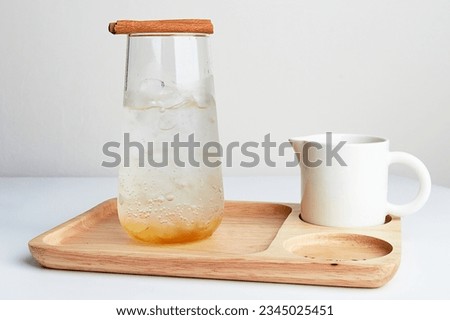 Iced sparkling soda in clear glass with cinnamon and white jug served on wooden tray placed on white table in cafe. Royalty-Free Stock Photo #2345025451