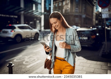 Young woman using a smart phone while walking on a sidewalk in the city Royalty-Free Stock Photo #2345035381
