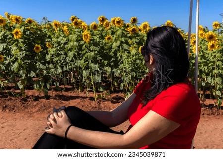 Portrait of a middle-aged woman with black hair and dark glasses sitting next to a field of sunflowers in Brazil
