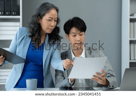senior asian business woman Discuss and advise Consulting young office workers about marketing plans, paperwork, financial information from the tablet to analyze and summarize the work in the office