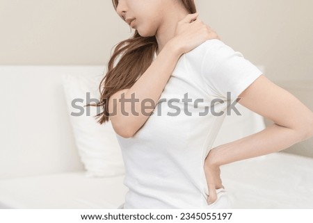 Pain body muscles stiff problem, asian young woman painful with back, neck ache from work hand holding massaging rubbing shoulder hurt, sore sitting on bed in room at home. Health care and medicine. Royalty-Free Stock Photo #2345055197