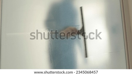 A man pastes a frosted coating on a glass door in a clinic to make the glass door opaque. Applying a matte coating to the glass.