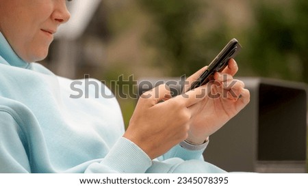 Close-up hands of woman with smartphone. Woman uses phone taps on touch screen, views news, information on Internet, chats in instant messengers. Close up female hands using black mobile phone. Royalty-Free Stock Photo #2345078395
