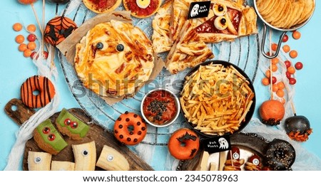 Fun Halloween dinner party table scene on a blue background. Top view. Pizza, pie, spaghetti and snacks.
