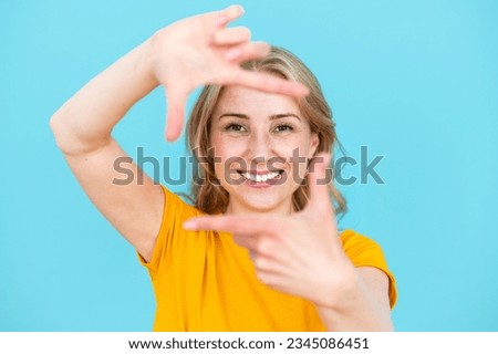 Cheerful toothily smiling woman making frame gesture isolated over blue studio background. Taking good shot, capturing moment, searching perfect angle