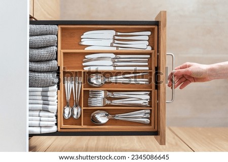 Top view of woman hand opening drawer with wooden cutlery tray. Separated section for knives, spoons, forks and linen towels. Storage of shiny silverware in the kitchen Royalty-Free Stock Photo #2345086645