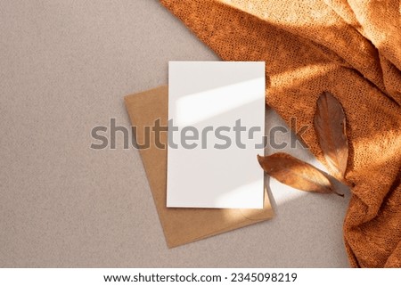 Blank paper card mock up, envelope, brown fall leaves, orange knitted textile on neutral beige background with aesthetic sun light shadow, autumn business branding template, wedding invitation design