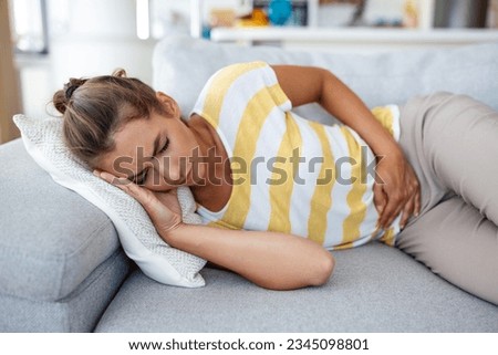 Woman lying on sofa looking sick in the living room. Beautiful young woman lying on bed and holding hands on her stomach. Woman having painful stomachache on bed, Menstrual period Royalty-Free Stock Photo #2345098801