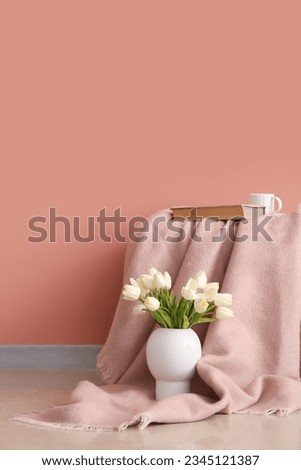 Plaid with book, cup and tulips in vase near pink wall