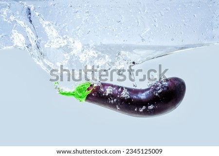 Whole eggplant dropped in water with splashes on gray