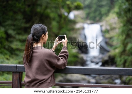 Woman take photo on cellphone with waterfall