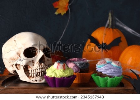 Board with delicious Halloween cupcakes and skull on wooden background, closeup