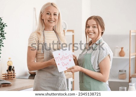 Young woman greeting her mother with card and gift in kitchen