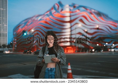 Young cheerful lady, using a tablet on the night-illuminated city street.