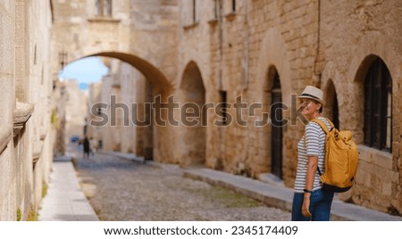 summer trip to Rhodes island Greece. Young Asian woman in striped tshirt and hat walks Street of Knights of Fortifications castle. female traveler visiting southern Europe. Unesco world heritage site Royalty-Free Stock Photo #2345174409