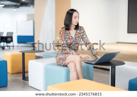 Side view of Asian female executives Head of the company business department like an employee Typing and looking at laptop sitting in the foyer of the home office wearing a beautiful floral suit