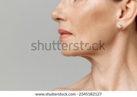 Double chin treatment. Cropped profile portrait with lips and chin neckline of middle-aged woman over grey studio background. Fashion, beauty, spa, cosmetology, skincare concept. Royalty-Free Stock Photo #2345182127