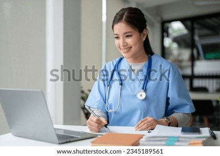 A beautiful and professional Asian female doctor is working on her medical cases on her laptop or making a video call medical consultation with a patient while sitting in her office.