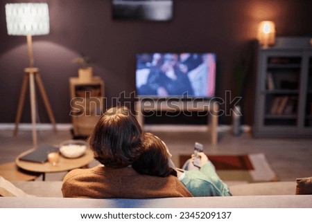 Back view of couple watching TV together sitting on sofa at home in evening, copy space Royalty-Free Stock Photo #2345209137