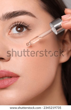Young woman applying essential oil onto face, closeup Royalty-Free Stock Photo #2345219735
