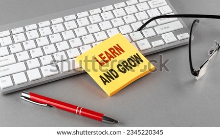 LEARN AND GROW text on sticky with keyboard, pen glasses on grey background