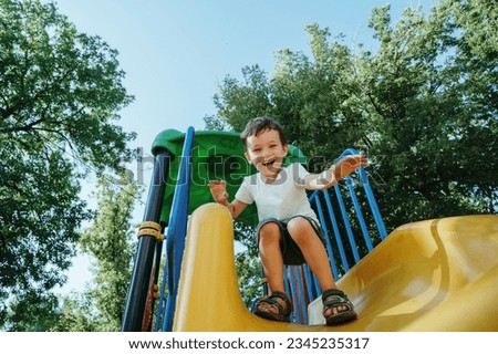 happy preschooler boy playing on a slide on the playground in summer Royalty-Free Stock Photo #2345235317