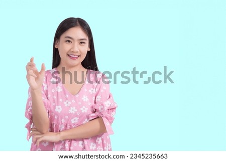 Young preetty Asian beautiful female with black long hair in pink shirt shows present something while isolated on light blue background.