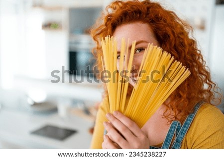 Photo of happy smiling woman looking at camera while hiding her face behind the spaghetti in the kitchen.