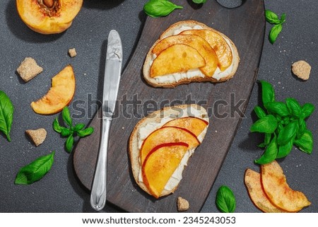 Fresh bread sandwiches with sweet peach slices, cream cheese and basil leaves. Good morning breakfast concept. Hard light, dark shadow, black stone concrete background, top view Royalty-Free Stock Photo #2345243053