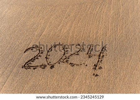 2024 hand written in sand on a beautiful beach. Textured sand with footprints and water.