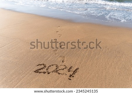 2024 hand written in sand on a beautiful beach. Textured sand with footprints and water. Royalty-Free Stock Photo #2345245135