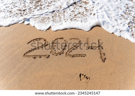 2024 hand written in sand on a beautiful beach. Textured sand with footprints and water. Royalty-Free Stock Photo #2345245147
