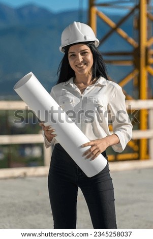 Smiling young female engineer in a white helmet holds a drawing of the project in her hands. Concept of construction, development, construction and architecture.