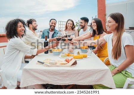 Happy multicultural group of young adult friends enjoying together celebrating a dining party with healthy food and toasting red wine glasses. Buddies having fun and cheering at lunch birthday feast Royalty-Free Stock Photo #2345261991