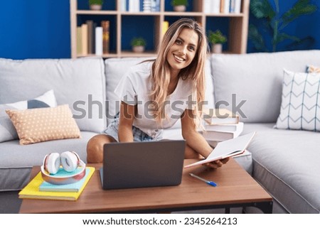 Young blonde woman student sitting on sofa reading notebook at home