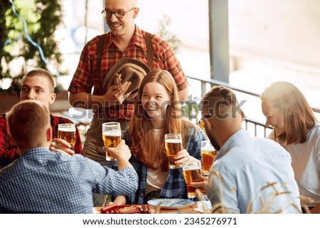 Group of cheerful young people, friends meeting at cafe, pub, spending time together, drinking beer. Celebration and fun. Concept pktoberfest, traditional taste, friendship, leisure time, enjoyment